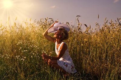 Side view of woman shielding eyes while hat while crouching amidst plants