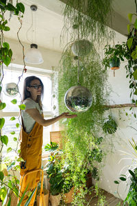 Side view of woman touching disco ball hanging in plant nursery