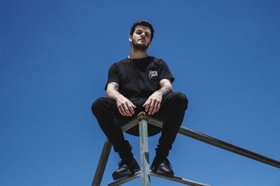 Low angle view of young man looking away against clear blue sky