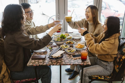 Cheerful male and female friends toasting drinks while sitting at restaurant