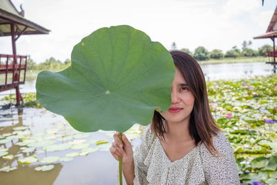 Portrait of young holding leaf by lake