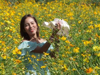 Portrait of smiling young woman with yellow flowers in field