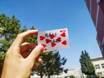 Cropped hand holding card against blue sky