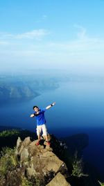 Man gesturing while standing on rocks against lake