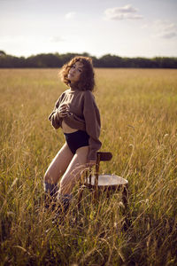 Fashion portrait of a curly-haired woman in a sweater and shorts sitting on a field with grass