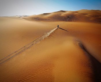 Tire tracks on sand dune in desert against clear sky