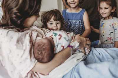 Side view of mother holding newborn son meeting siblings