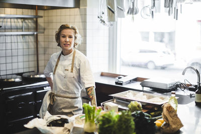 Portrait of confident female owner standing by kitchen counter at restaurant