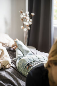 A woman lies on the bed with pencils in her jeans pocket.