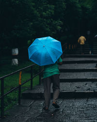 Rear view of woman walking on wet umbrella during rainy season