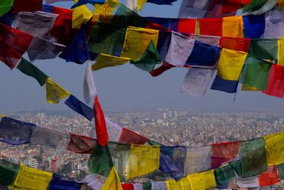 Multi colored flags hanging in city against sky