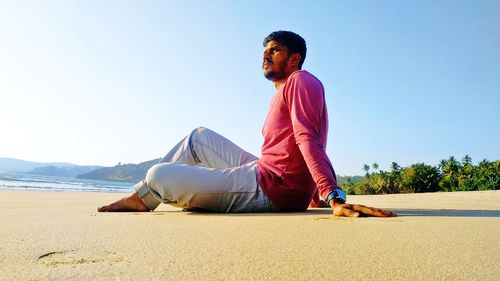 Young man sitting on beach against clear sky