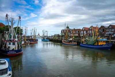 Boats moored at harbor in city against sky