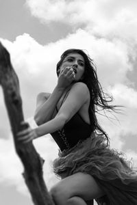 Low angle view of woman holding tree branch against cloudy sky