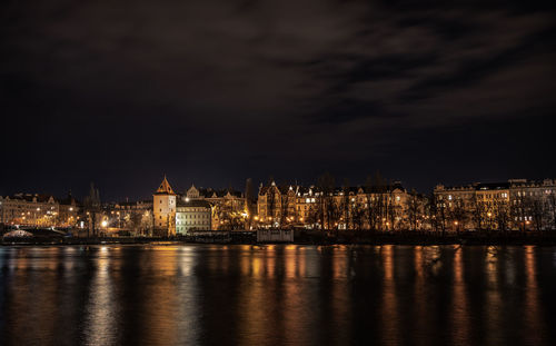 Illuminated city by river against sky at night