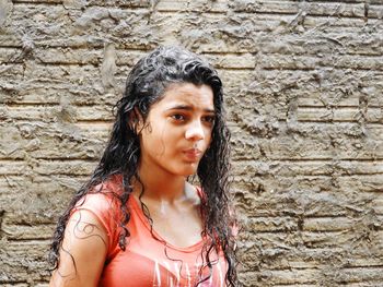 Thoughtful wet teenage girl standing against concrete wall