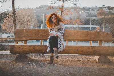 Full length of smiling young woman sitting on bench