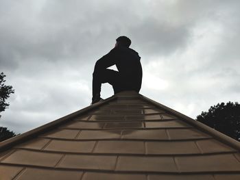 Low angle view of silhouette man sitting against sky