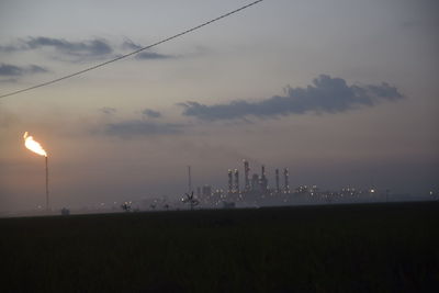 Fire emitting from smoke stack at industrial site against sky