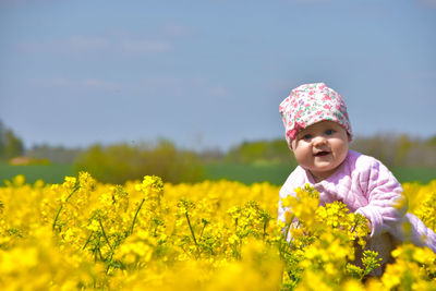 One happy 9 month old baby girl in rapeseed blooming field in pink clothes 