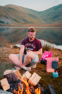 Portrait of young man sitting on wood against mountains