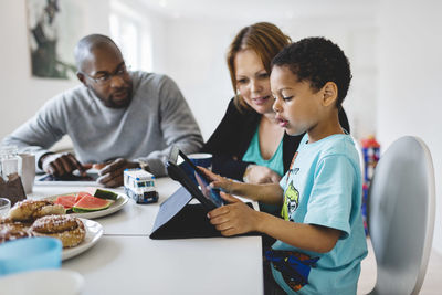 Parents looking at son using digital tablet in house