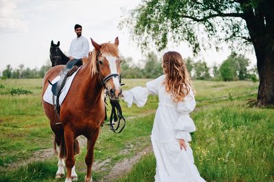 Wedding couple horseback riding on field