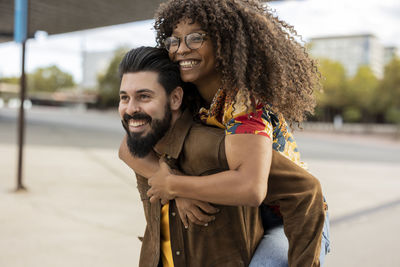 Happy man giving piggyback ride to girlfriend at footpath