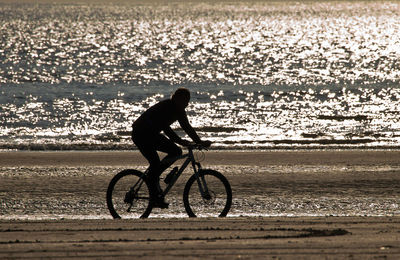 Side view of silhouette man riding bicycle on beach