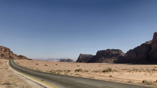 Road leading towards mountains against clear sky