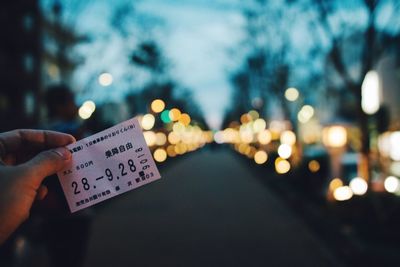 Close-up of hand holding illuminated ticket