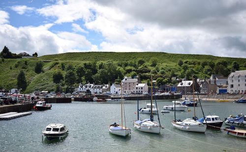 Sailboats moored on harbor by buildings in city against sky