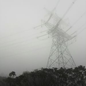 Low angle view of electricity pylon against sky during foggy weather