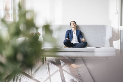 Smiling businesswoman sitting on couch with beverage