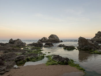 Rocks on beach against sky during sunset