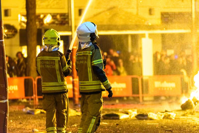 Rear view of firefighters standing on road at night