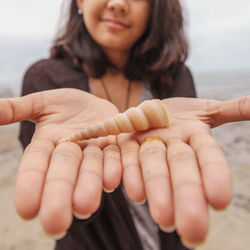 Midsection of girl showing shell while standing at beach