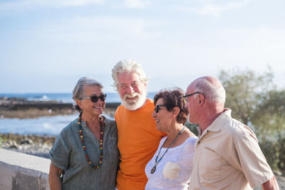 Smiling senior friends talking at bridge against sky