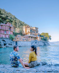 People sitting by sea against clear sky