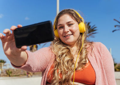 Portrait of smiling woman taking selfie against sky