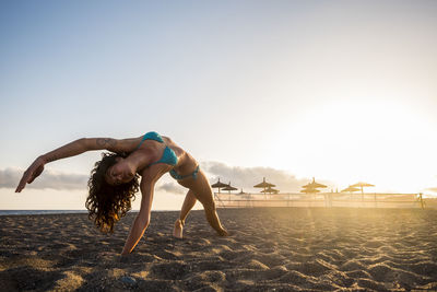 Full length of woman exercising at beach against sky
