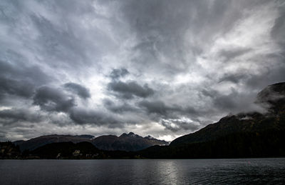 Scenic view of lake and mountains against storm clouds