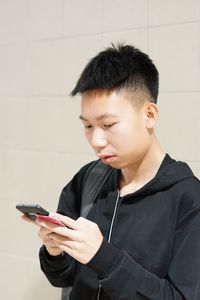 Young man using mobile phone against wall