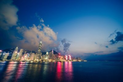 Illuminated city by sea against sky