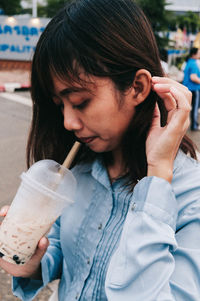 Close-up of woman having drink while standing on footpath