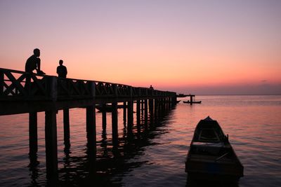 Silhouette pier on sea against orange sky
