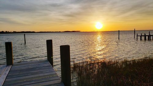 Wooden posts in sea against sky during sunset