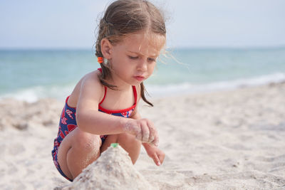 Cute girl crouching on beach against sky