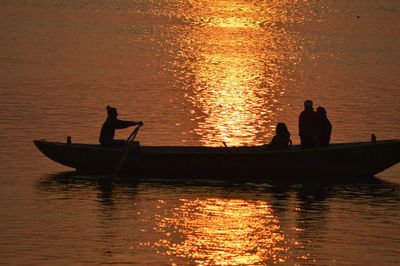 Silhouette people sailing on boat in lake during sunset