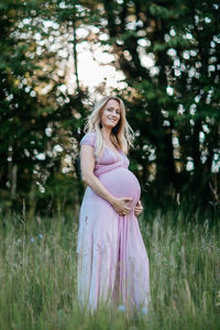 Happy pregnant woman standing on field